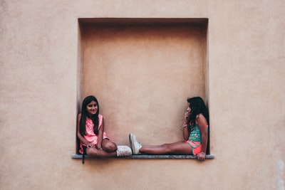两个穿粉红色和绿色衬衫的女孩坐在墙上的架子上